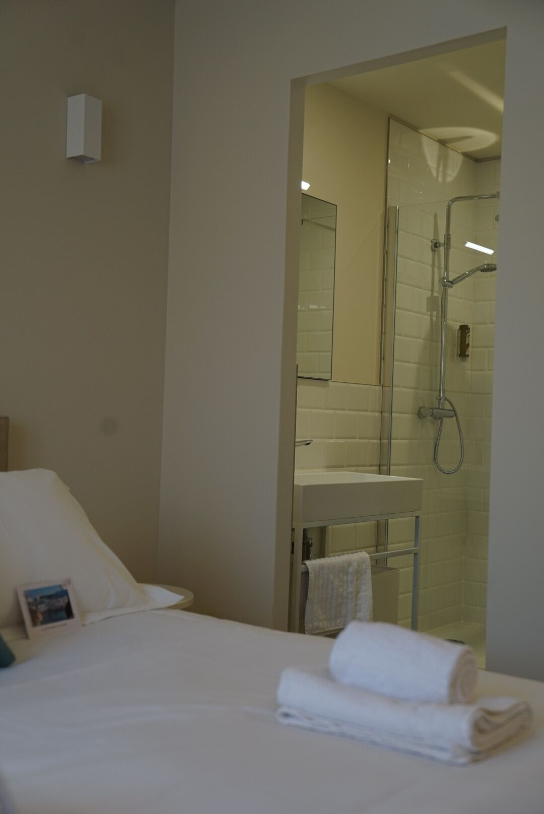 Ein Hotelzimmer mit Bett, einem durch eine Glastrennwand sichtbaren Badezimmer und einem kleinen Handtuch auf dem Bett.