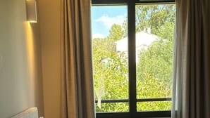 Una habitación de hotel con cama, mesita de noche, ventana con cortinas y vistas a zonas verdes.