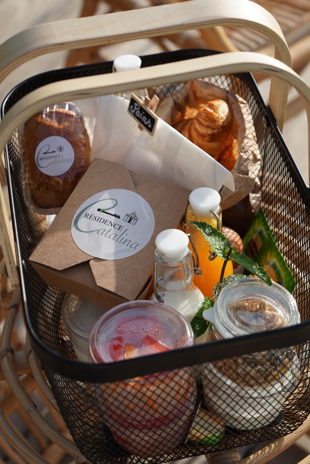 A basket containing a bottle of wine, a jar of jam, a jar of honey, a bottle of orange juice, and a small container of milk.