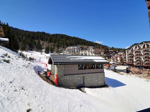 A ski resort with a stone building, snow-covered slopes, and a mountain backdrop.