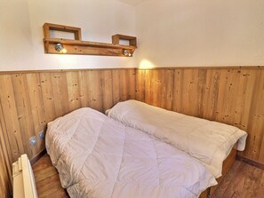 A small room with wooden paneling, two beds, a shelf with lights, and a thermostat.