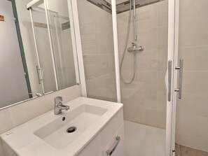 A bathroom with a white sink, a mirror, and a shower with a handheld showerhead.