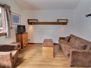A cozy living room with a wooden TV stand, a brown sofa, a wooden coffee table, and a painting on the wall.
