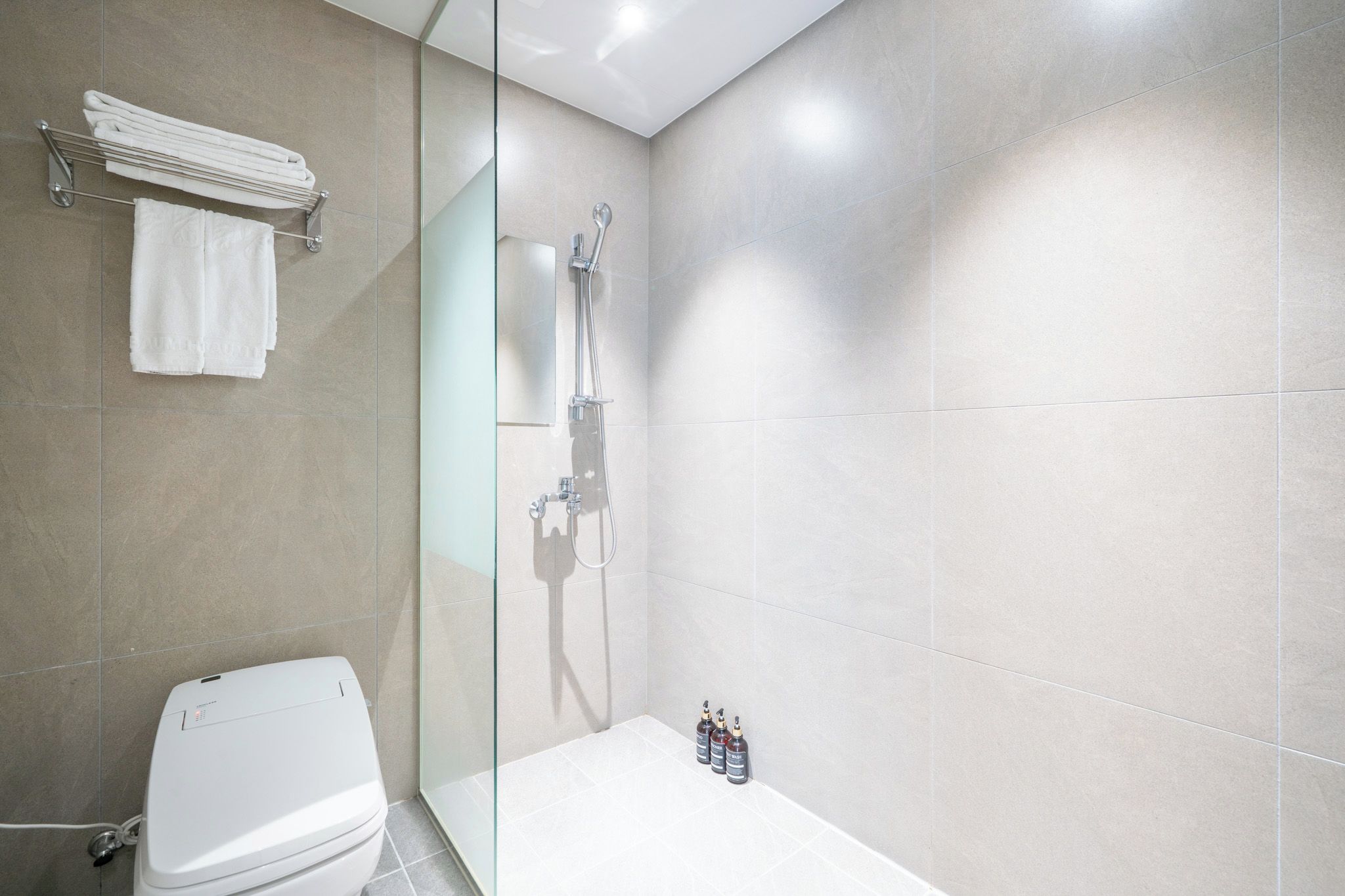 A modern bathroom with a glass shower enclosure, a white toilet, and a glass partition.