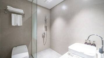 A modern bathroom with a glass-enclosed shower, a white toilet, and a sink with toiletries.