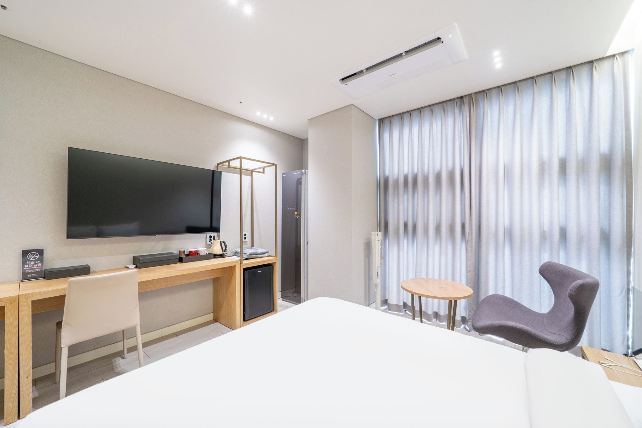 Hotellihuone, jossa on sänky, työpöytä, tuoli, televisio ja ikkuna, jossa on verhot.