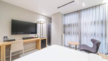 A hotel room with a bed, a desk, a chair, a television, and a window with curtains.