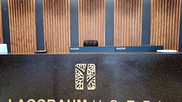 A reception desk with a wooden panel background and clocks displaying different time zones. The name "LAGOBAUM HOTEL" is prominently displayed on the desk.