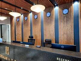 Zona de recepción de un hotel con paneles de madera, varios relojes en la pared y un mostrador con una computadora y un teléfono.