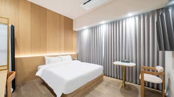 A modern hotel room with a large bed, a bedside table, a chair, a small round table, and a television.