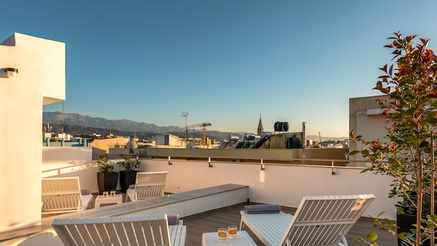 Una terraza en la azotea con sillones blancos, una mesita y dos vasos de bebida.