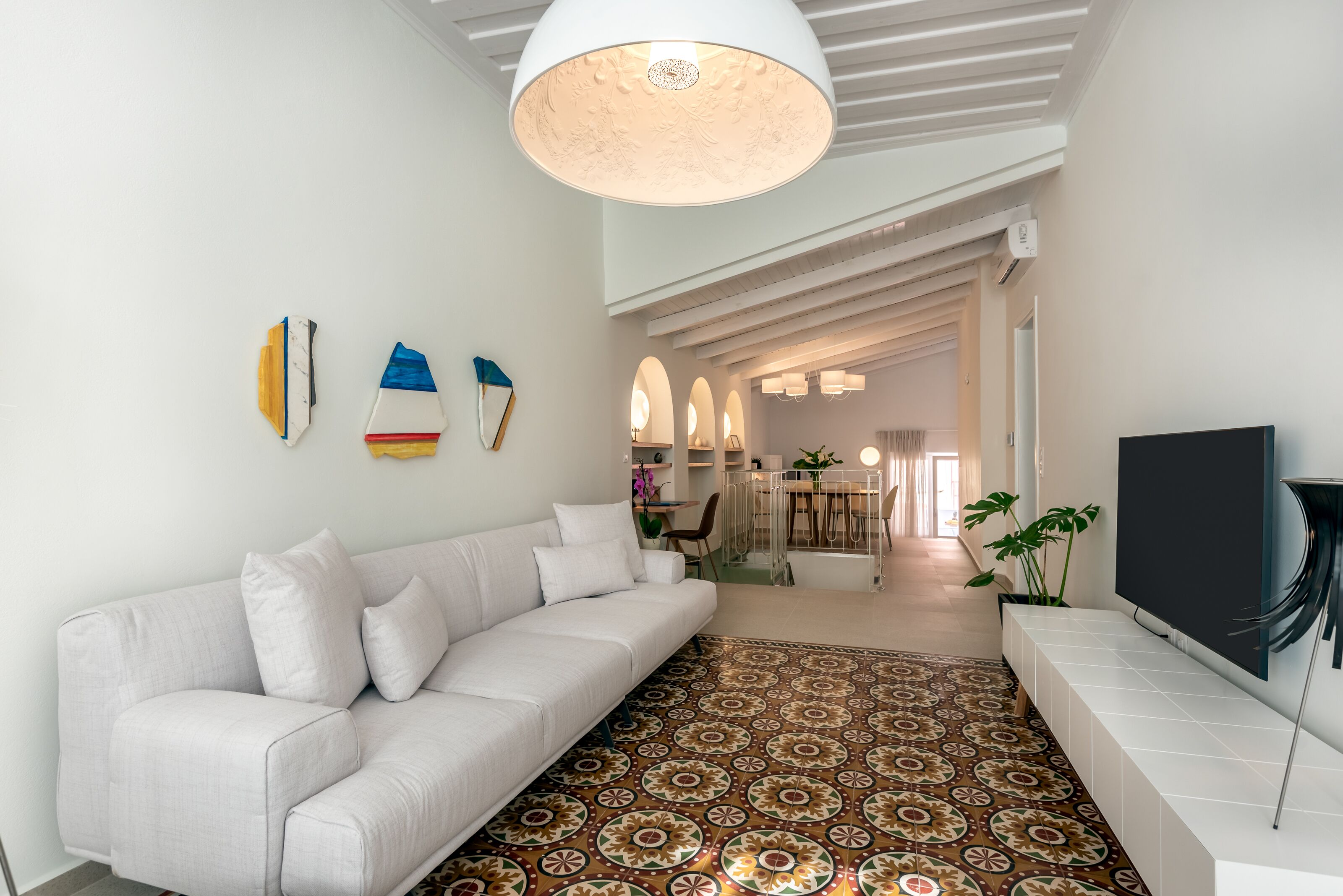 A modern living room with a white sofa, patterned rug, and a TV on a white stand.