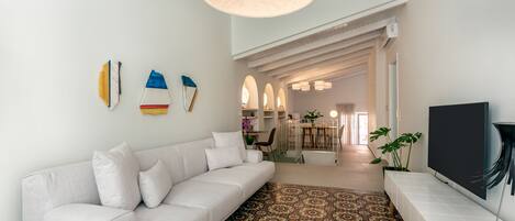 A modern living room with a white sofa, patterned rug, and a TV on a white stand.