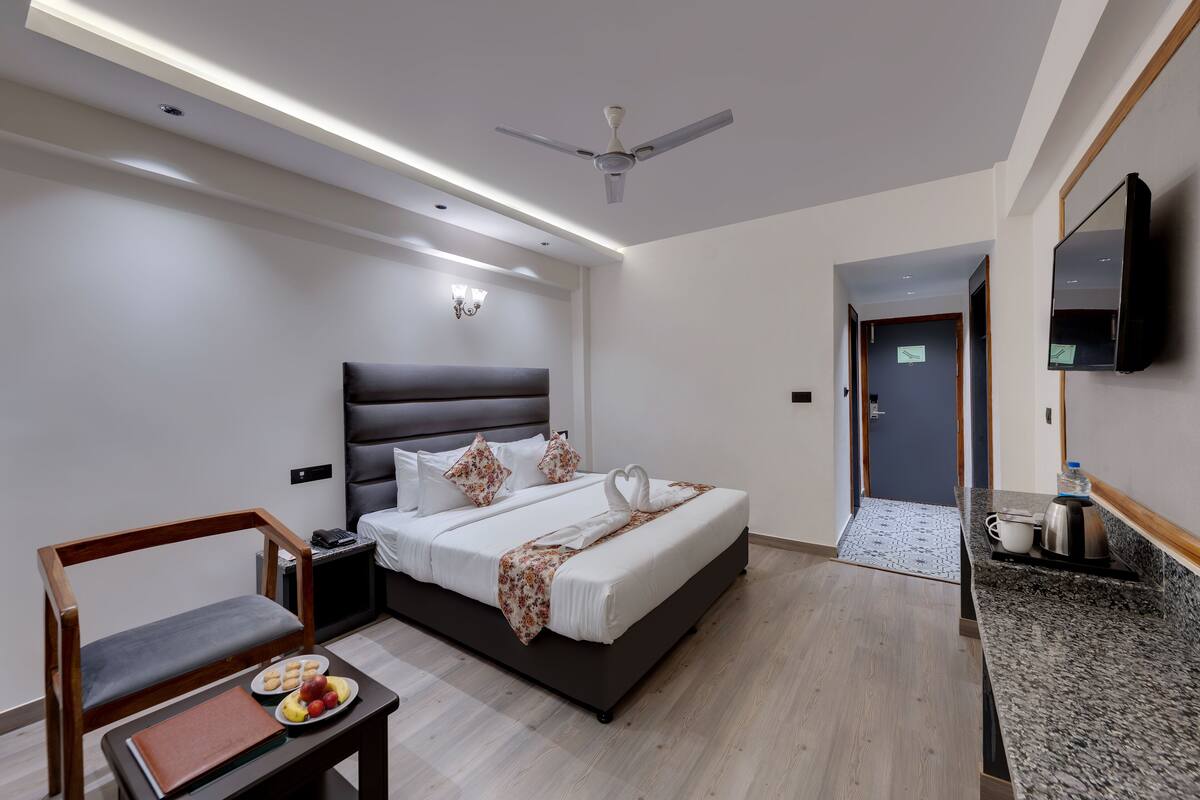 Una habitación de hotel moderna con una cama, mesita de noche, silla y una pequeña zona de kitchenette.
