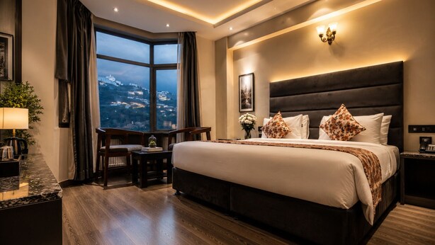 Habitación de hotel con una cama grande, un escritorio, una silla, vistas a la ciudad y una mesita de noche con un teléfono.