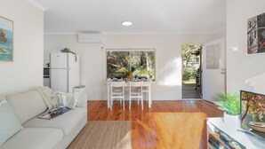 Un salón espacioso con un sofá blanco, una zona de comedor con mesa y sillas, y una cocina con refrigerador.