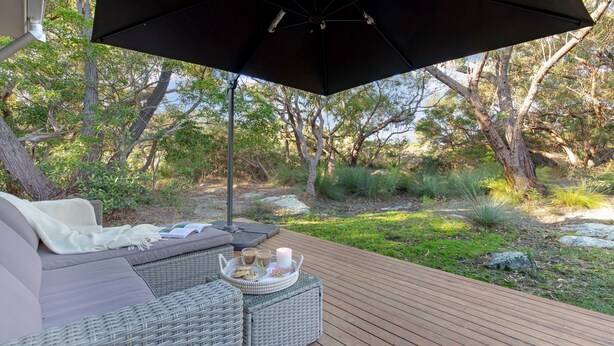 Un espacio al aire libre con un sofá de mimbre, una mesa con una vela y una bandeja de aperitivos.