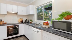 Cocina moderna con armarios blancos, horno Bosch, lavavajillas, fregadero y ventana con vistas a árboles.