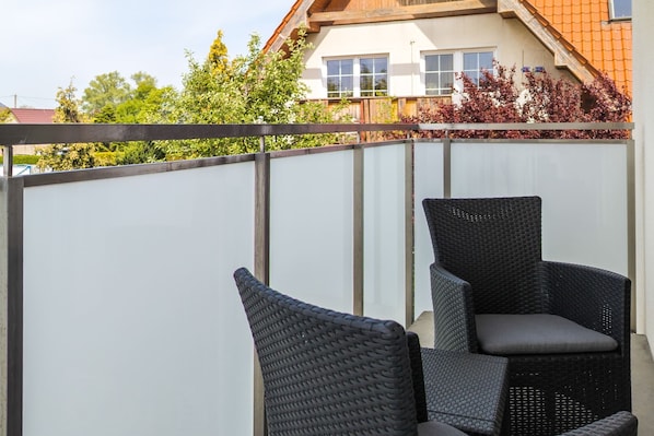 Ein Balkon mit zwei Korbstühlen und einem weißen Sichtschutz.