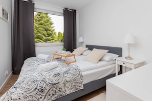 A bedroom with a bed, bedside table, lamp, and a window with curtains.