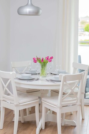 A round dining table with white chairs, a vase with pink flowers, and a pendant light.
