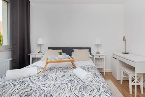 A modern hotel room with a bed, bedside tables, a desk, and a window with curtains.