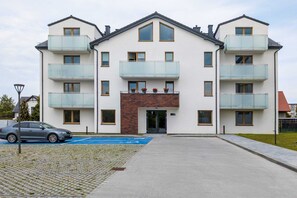 Ein mehrgeschossiges Wohngebäude mit Balkonen, einem Parkplatz und einem gepflasterten Eingangsbereich.
