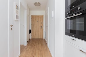 A hallway with a wooden door, white walls, and a black oven.
