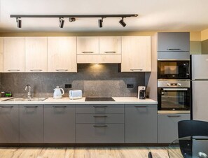 A modern kitchen with grey cabinets, a built-in oven, and a coffee maker.