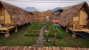 Una cabaña rústica con techos de paja, zona de fogata, zona de picnic, bar y letrero de hoguera.