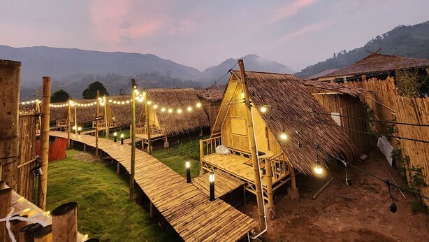 Pueblo rústico con chozas de techo de paja conectadas por pasarelas de madera, bajo un cielo crepuscular.