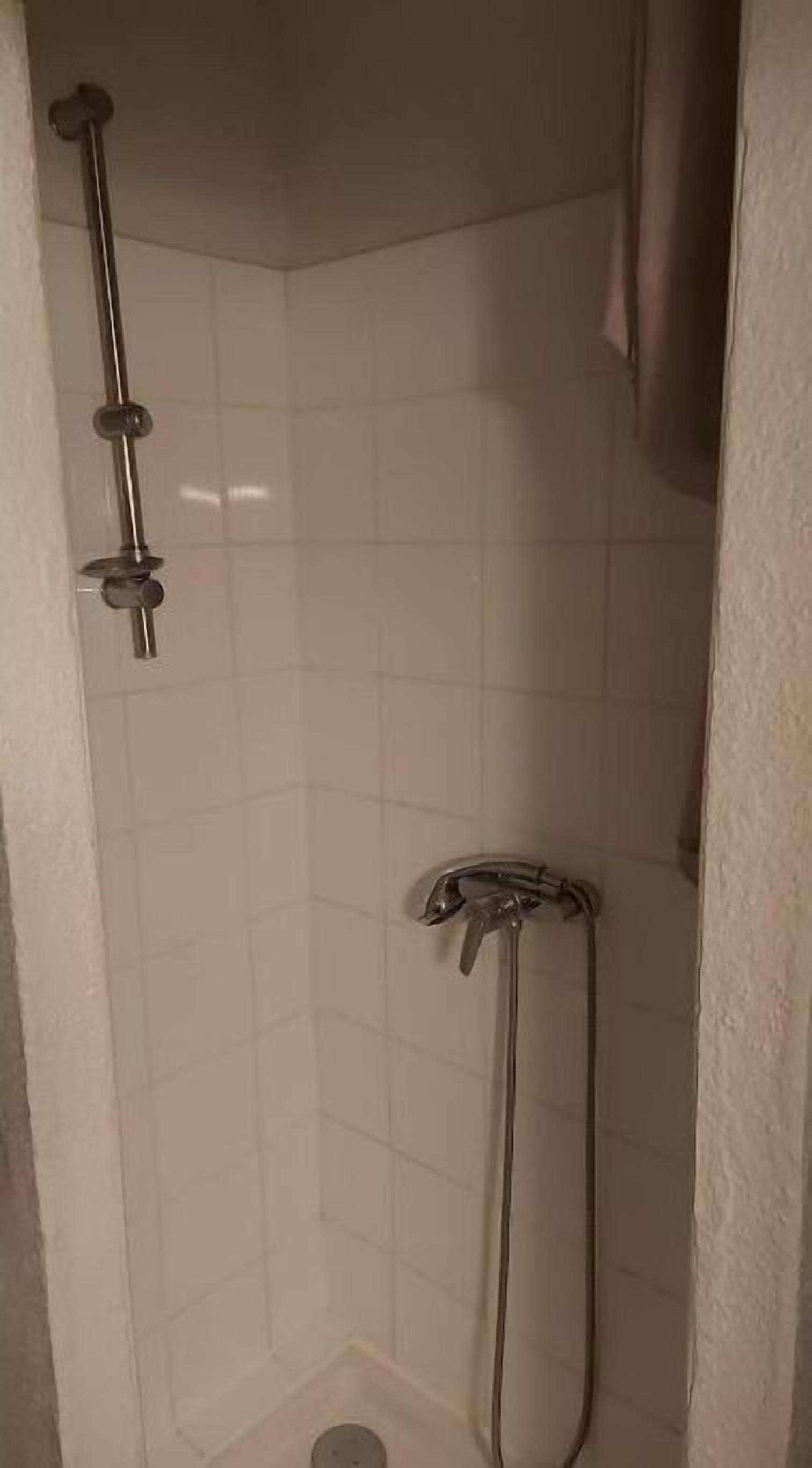 A small, enclosed shower area with white tiled walls and a showerhead mounted on the wall.