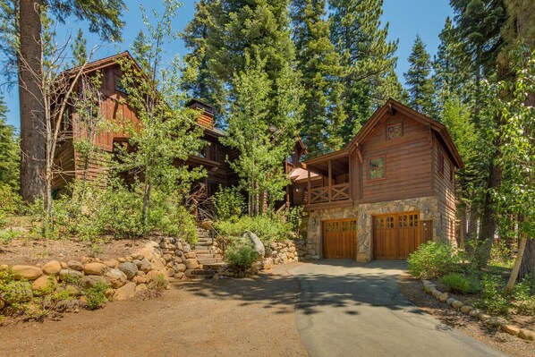 A rustic log cabin with a stone foundation, a wooden porch, and a stone pathway leading to the entrance.
