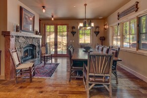 Une salle à manger spacieuse avec une cheminée en pierre, un plancher en bois et de grandes fenêtres donnant sur l’extérieur.