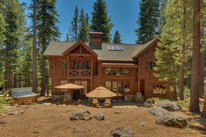 A large wooden cabin with a spacious patio, multiple windows, and a hot tub.