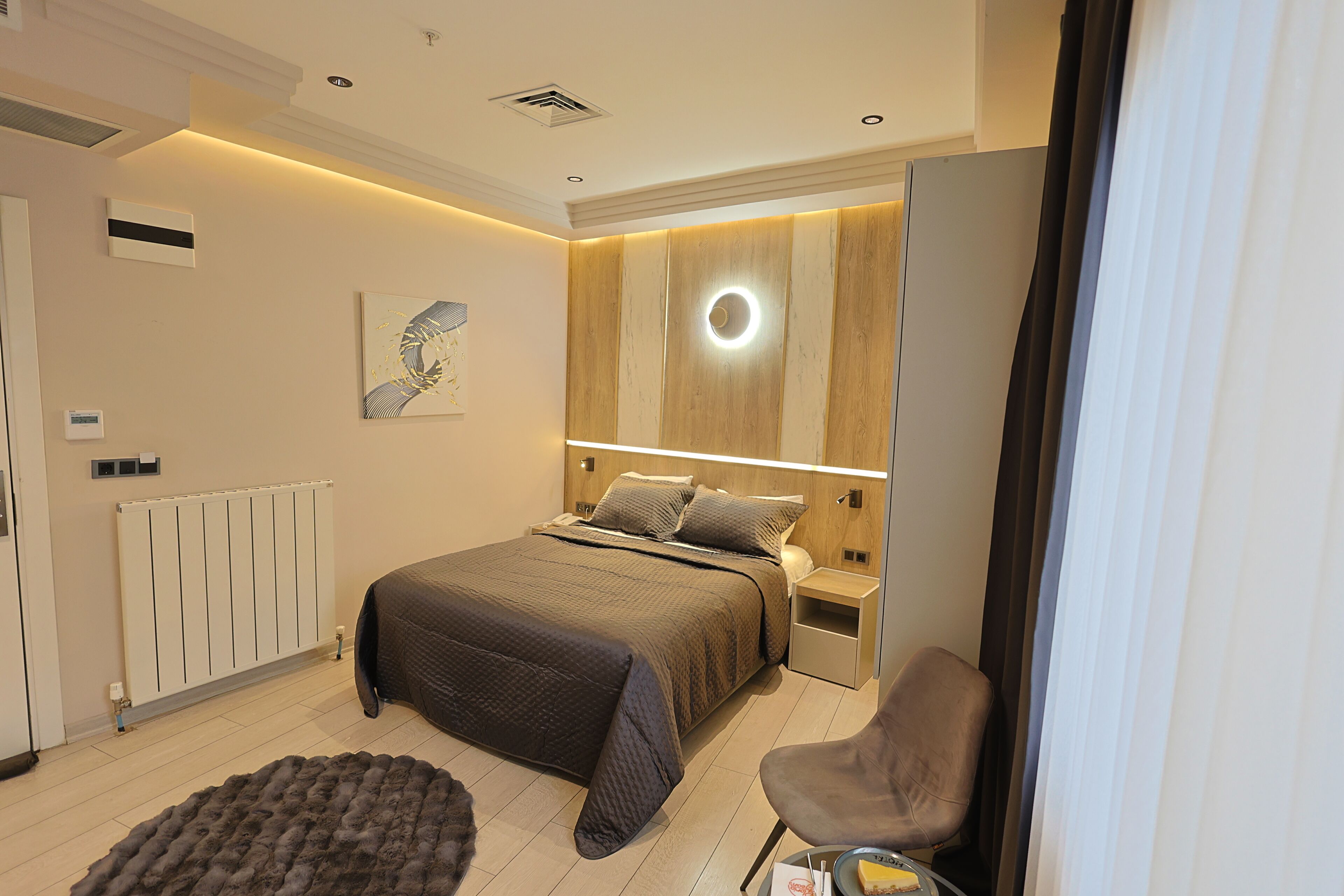 Una camera da letto moderna con un letto, comodini, una sedia, un termosifone e un lampadario a parete.