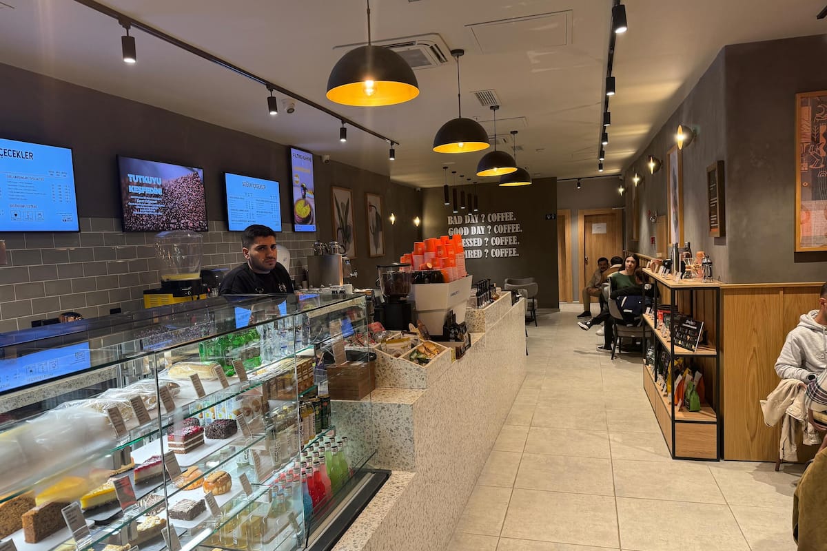 L'intérieur d'un café moderne présente un comptoir où sont exposées des pâtisseries et des boissons, un tableau affichant le menu, ainsi qu'un espace réservé aux clients.