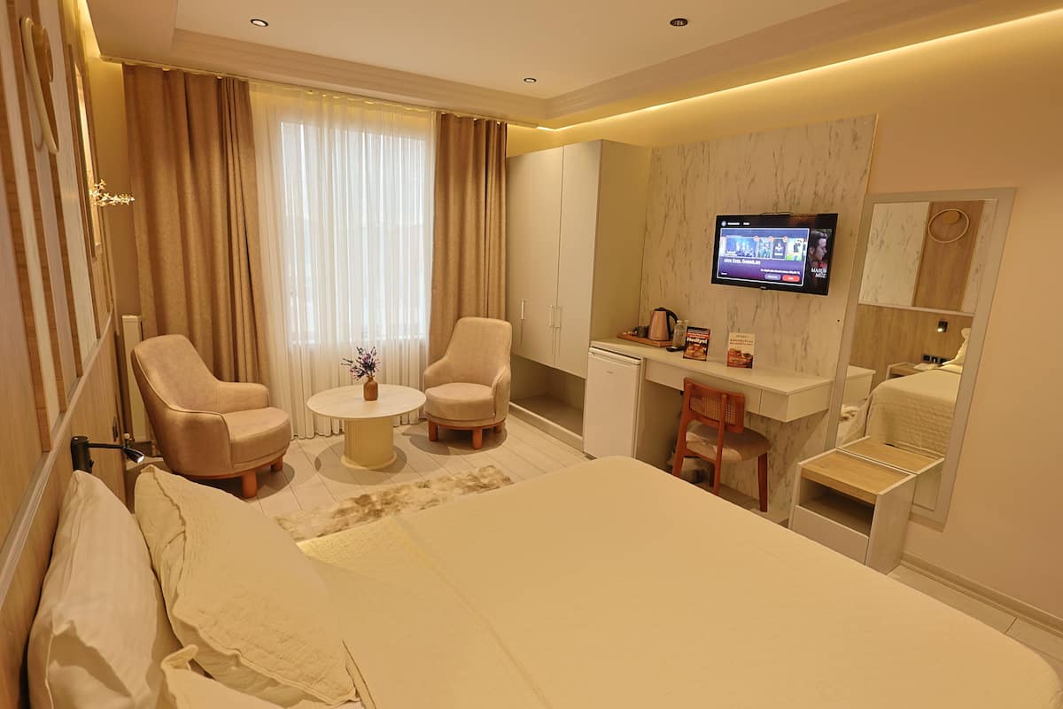 Une chambre d’hôtel comprenant un lit, deux fauteuils, une petite table ronde, un bureau avec une chaise, une télévision et une armoire.