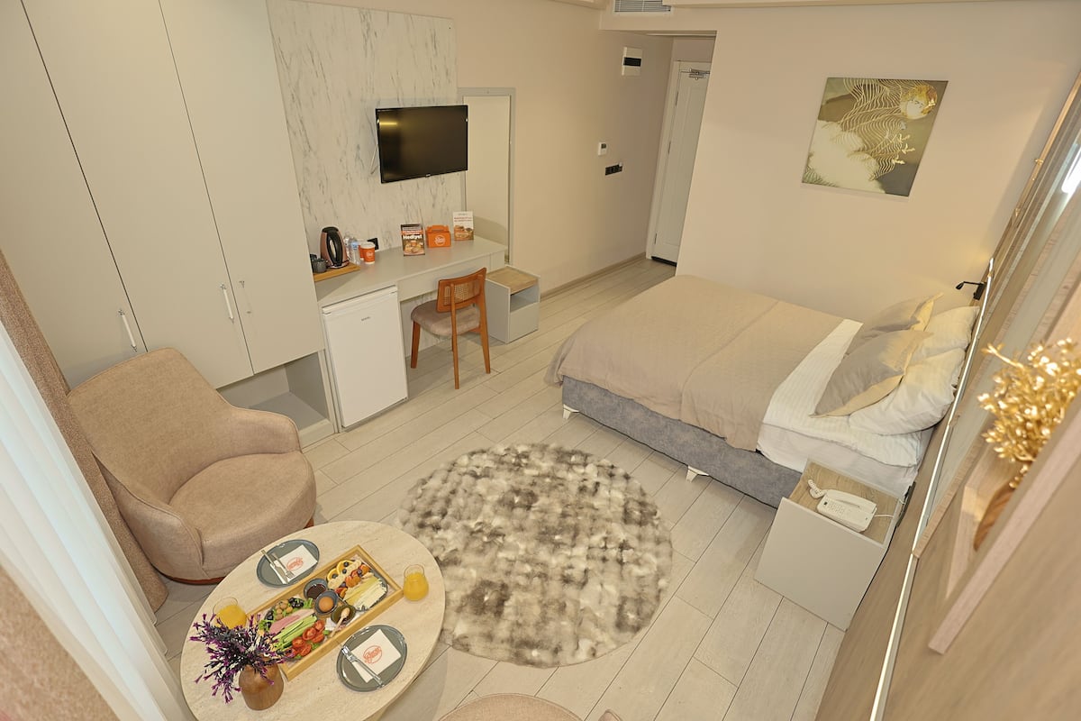 Quarto moderno com cama, escrivaninha, cadeira e uma pequena mesa com um vaso e frutas.