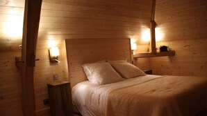 A wooden cabin bedroom with a bed, bedside lamps, and a shelf with a small house model.