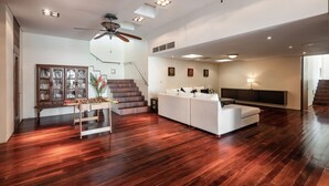 Un ampio soggiorno con pavimento in legno, un divano bianco, una ventola a soffitto e una scala che conduce a un altro livello.