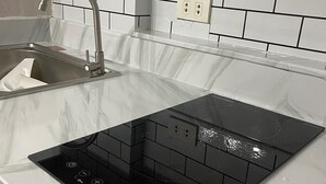 Una cucina con piano cottura a induzione nero, lavello in acciaio inossidabile e un top in marmo bianco.