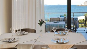A dining area with a table set for two, a view of the sea, and a hanging light fixture.