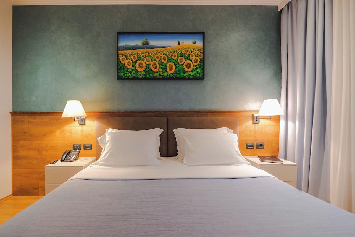 Ein Hotelzimmer mit einem großen Bett, zwei Nachttischlampen, einem Gemälde einer Sonnenblumenwiese und einem Holzkopfende.