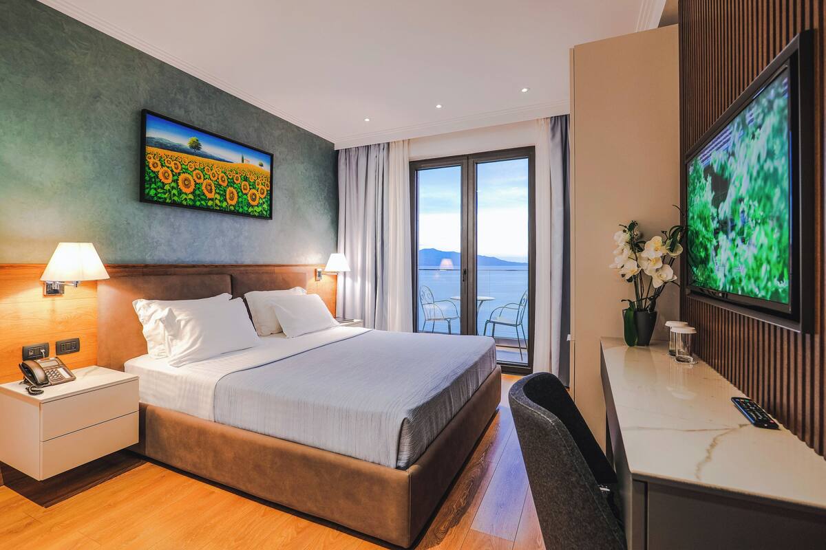 Ein Hotelzimmer mit Bett, Schreibtisch, Fernseher und einem Sonnenblumenbild an der Wand.
