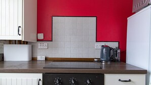 Eine Küche mit roter Wand, weißen Schränken, einem Herd und einem Wasserkocher.