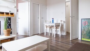 Ein heller, weißer Raum mit Esstisch und Stühlen, einer kleinen Pflanze und einem Bild an der Wand.
