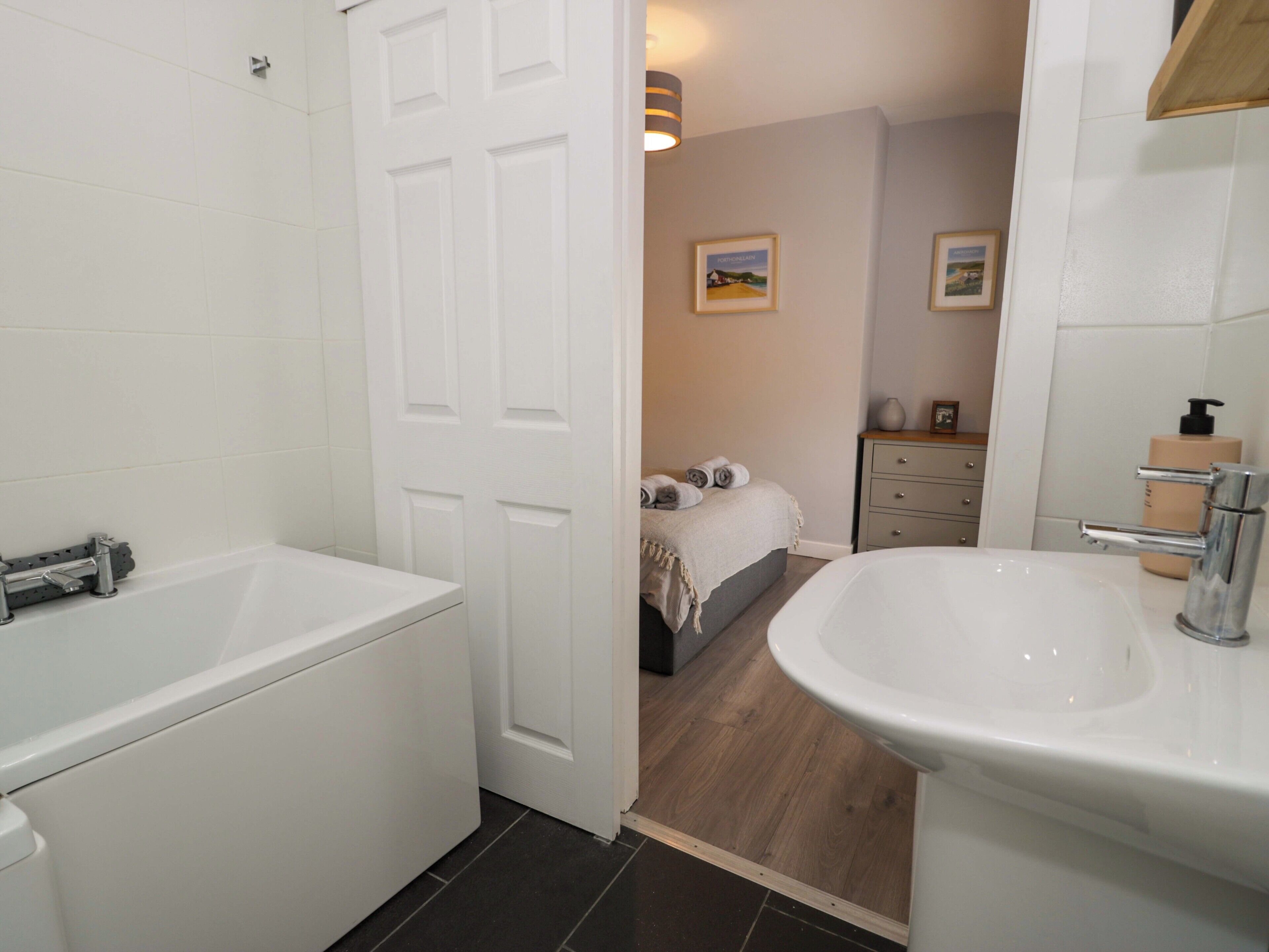 A bathroom with a bathtub, a sink, and a door leading to a bedroom with a bed and a dresser.