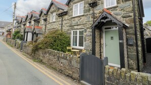 A row of stone houses with traditional architecture, a stone wall, and a road with a double yellow line. - Y Bwthyn (Llanbedr)
