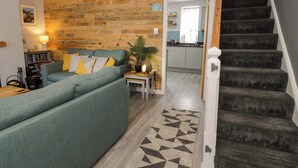 A living room with a sofa, a staircase, and a kitchen in the background. - Y Bwthyn (Llanbedr)
